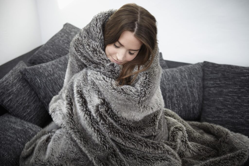 young woman on couch wrapped in fur blanket