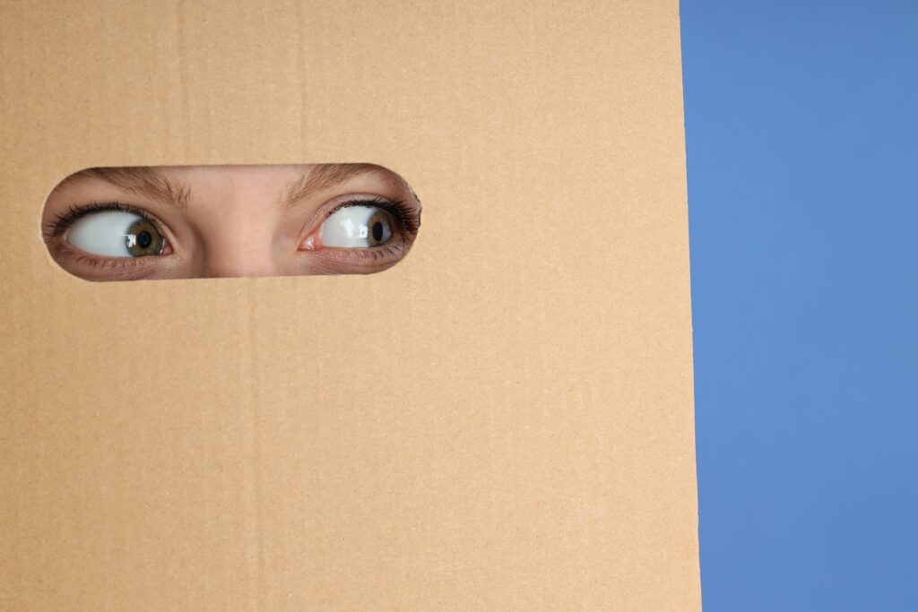 Hole in cardboard with young woman eyes 